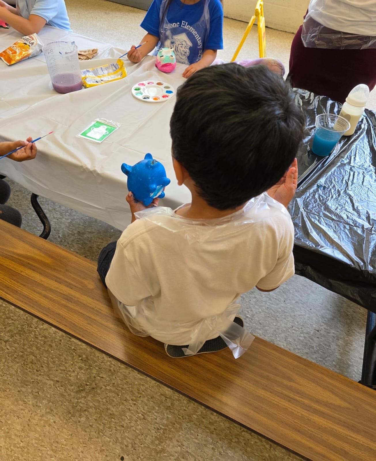 back of kid's head at table with 2 other kids painting, faces not shown