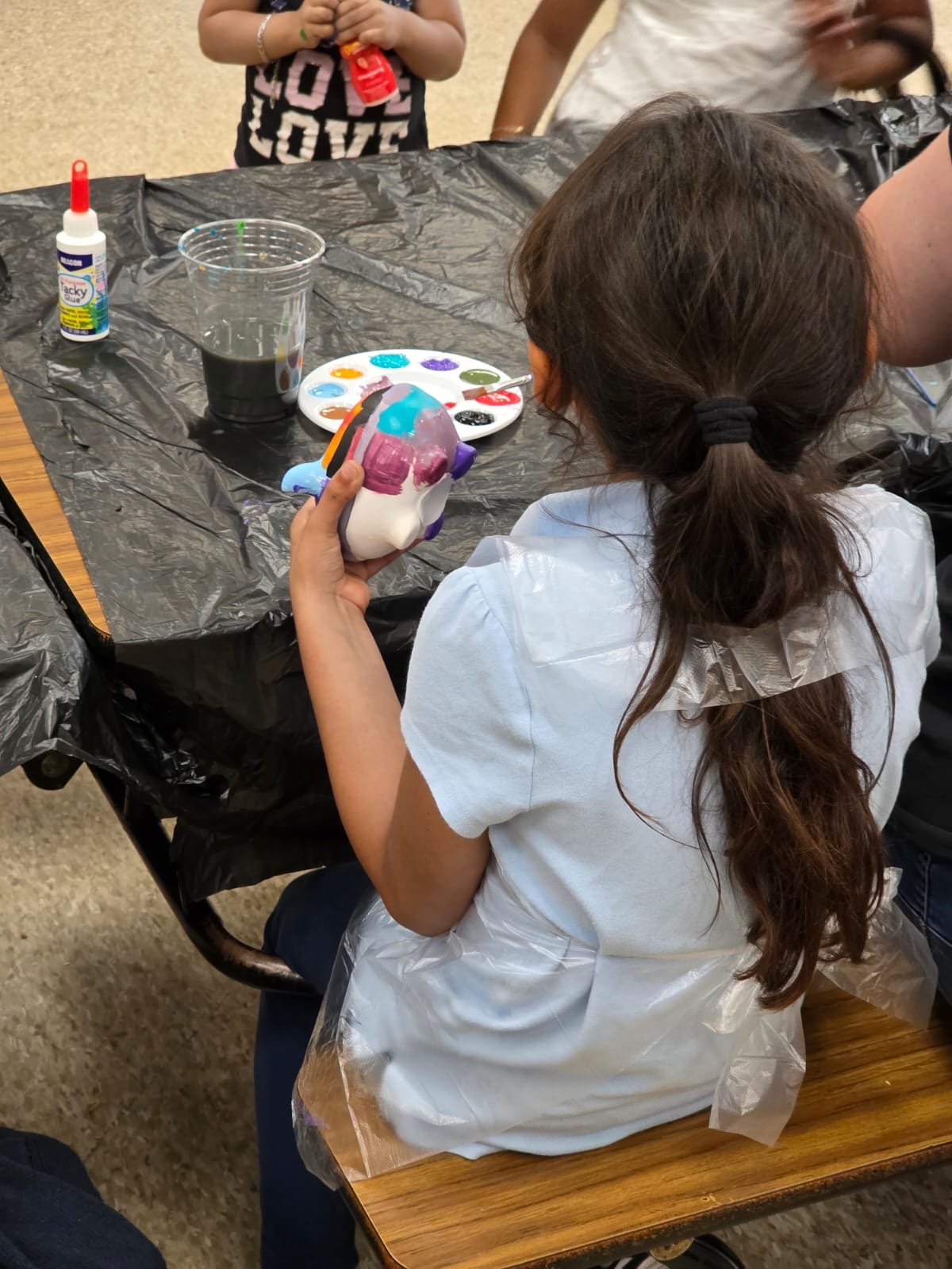 Shows back of child painting a piggy-bank