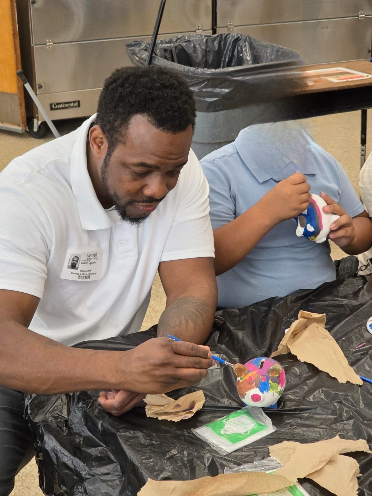 black man painting a piggy-bank with a kid whose face is not shown