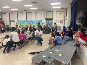 classroom half filled with people at tables and on steps to a stage